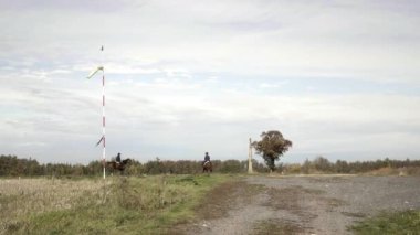 Günbatımı gökyüzü arka planında Windsock. Rüzgarda parlayan hava durumu aleti. Meteoroloji rüzgar çorabı, rüzgar hızı. Arka planda iki binici at sırtında