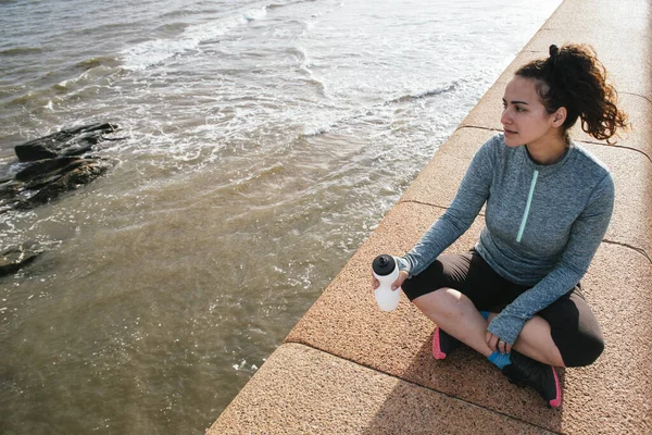 Jovem Latina Exausta Sentado Olhando Para Mar Com Uma Garrafa — Fotografia de Stock