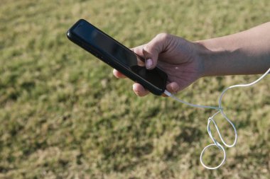 Beyaz kadın elinde kulaklıkla bir cep telefonu tutuyor.