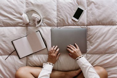 beyaz, latin, beyaz kız yatakta oturuyor, bilgisayarını açıyor. Serbest çalışan biri evde çalışıyor. cep telefonu, dizüstü bilgisayar, dizüstü bilgisayar, not defteri, tablet, harici disk ve kulaklıklar ile yatağın üzerinde..