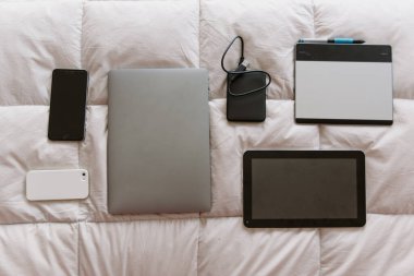 Serbest çalışan biri yatağa cihaz sipariş etti. cep telefonu, cep telefonu, harici disk, tablet, bilgisayar, not defteri, defter, kulaklık, beyaz yastıklı.
