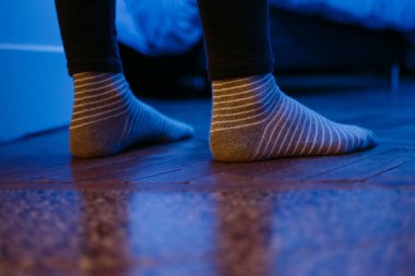 Biri odasına giriyor, kapıda, çizgili gri ve beyaz çoraplı, mavi ışıklı, yakın plan.