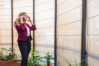 Baş ağrısıyla cep telefonuyla konuşan genç bir iş kadını. O, evde bitki ve pencereli resmi giysiler giyiyor..