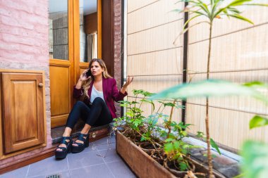 Kafkasyalı öfkeli kadın cep telefonuyla bağırıyor, kızgın, resmi kıyafetler giyiyor, yerde bitkilerle oturuyor..