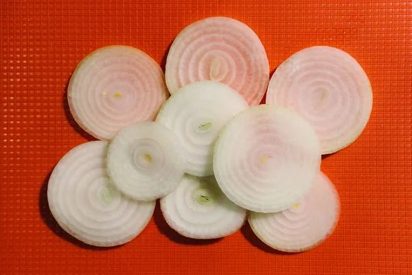 White onion slices on a orange chopping board. Top view.