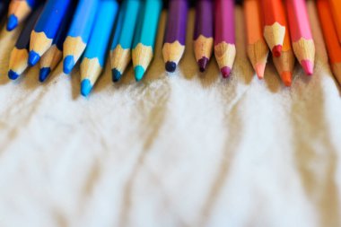 Bej bir kumaşta parlak renkli kalemler. Mavi, gökyüzü mavi, yeşil, menekşe, pembe, kırmızı ve turuncu. Çocuklar için okul malzemeleri. Boşluğu kopyala.