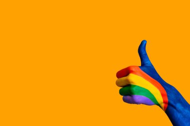 Turuncu arka planda, başparmağı havada renkli bir el. Boşluğu kopyala.