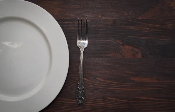 Empty white plate with a fork on a wooden brown surface — ストック写真