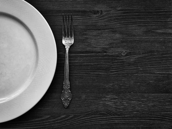 Lege witte plaat met een vork op een houten oppervlak, de zwarte en de whi — Stockfoto