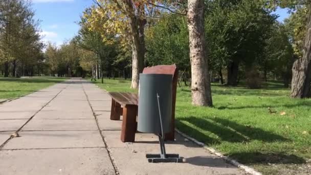 Urne grise fer à côté d'un banc en bois dans un parc municipal — Video