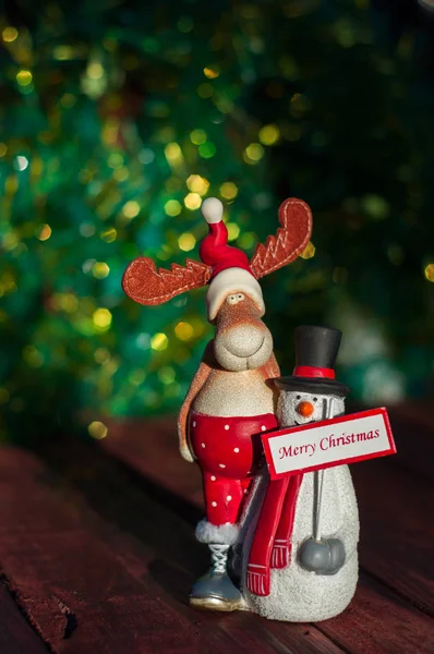 Alce y muñeco de nieve con un signo de saludo feliz Navidad en una madera — Foto de Stock