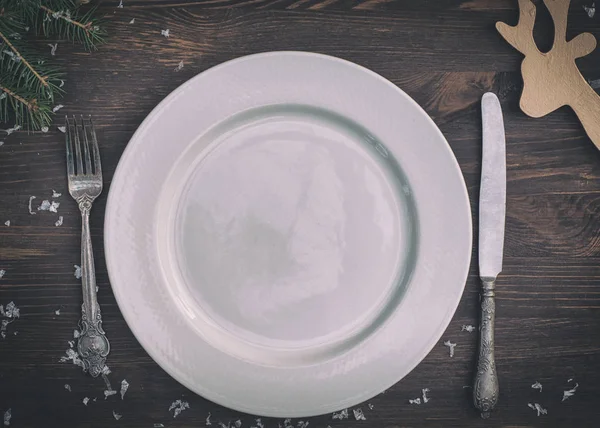 Белая тарелка с серебряным ножом и вилкой на коричневой деревянной поверхности С — стоковое фото