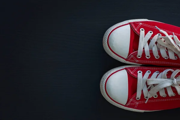 Rood textiel jeugd sneakers op een zwarte houten ondergrond — Stockfoto