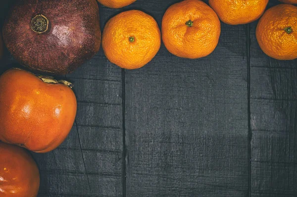 Mandalina, nar ve bir siyah ahşap yüzeyde Trabzon hurması