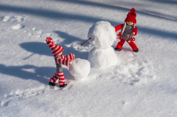 Два маленьких деревянных человека в сцене создания снеговика среди — стоковое фото