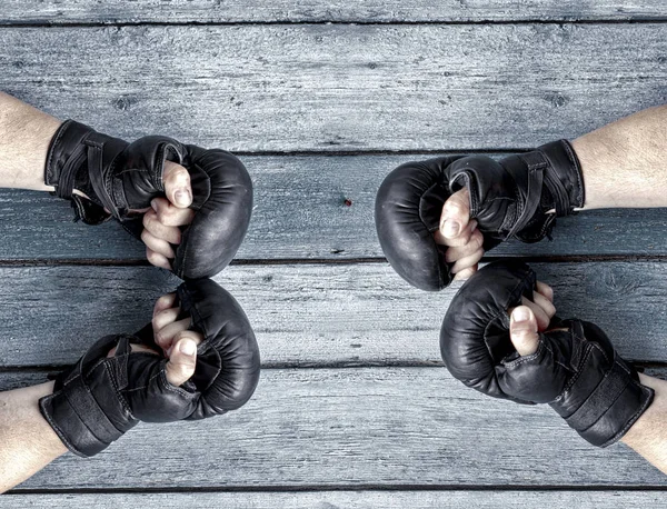 Two pairs of human hands in black leather boxing gloves facing e