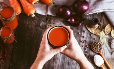 Bir demir kupa ile havuç suyu tutan iki eller 