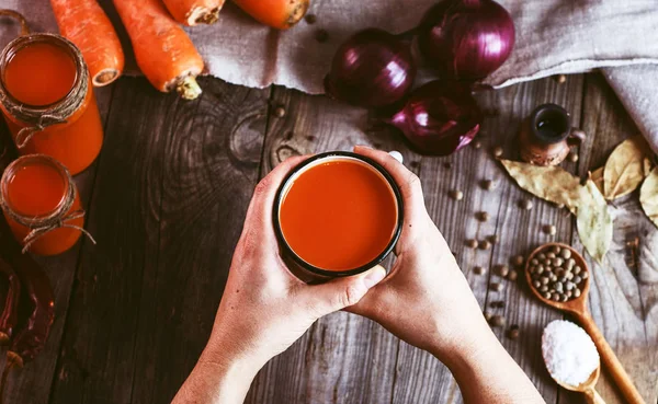 Bir demir kupa ile havuç suyu tutan iki eller 