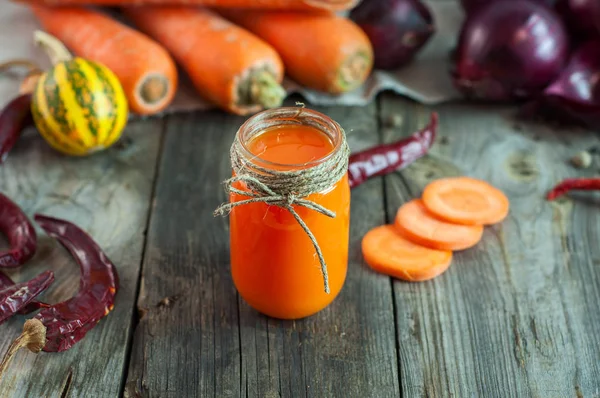 Морковный сок в прозрачной маленькой банке среди свежих овощей — стоковое фото