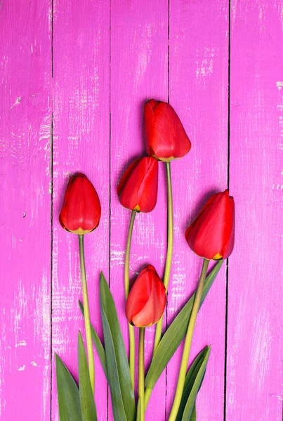 粉红色的木制表面上五个红色郁金香 — 图库照片