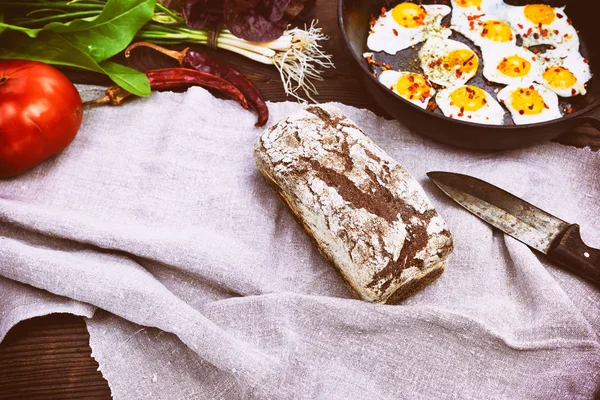 Буханка ржаного хлеба и жареные яйца в черной сковороде — стоковое фото
