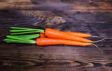 Kahverengi ahşap bir masa üzerinde üç taze turuncu havuç