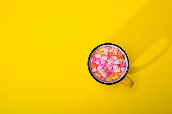 Cocoa with marshmallow slices in a yellow mug, top view, empty s