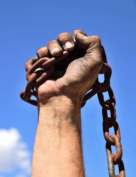 man's hand wrapped in an iron rusty chain lifted up against a bl