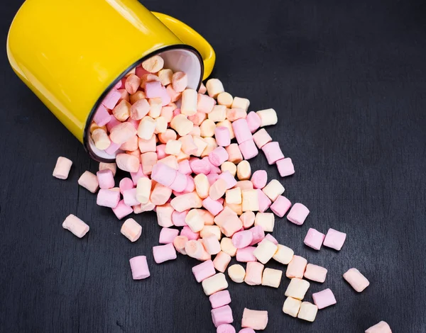 Marshmallows coloridos espalhados de uma caneca amarela — Fotografia de Stock