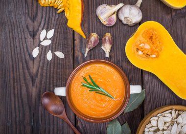 bir tahta kaşıkla bir seramik tabak içinde balkabağı çorbası 