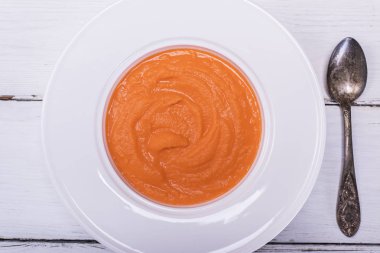 bir beyaz yuvarlak tabak ve bir demir kaşık balkabağı çorbası