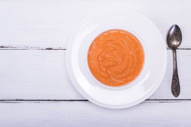 bir beyaz yuvarlak tabak ve bir demir kaşık balkabağı çorbası 