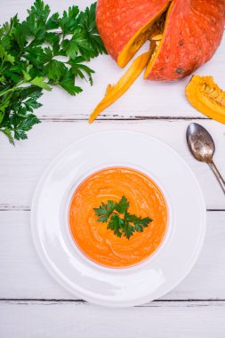 Bir yuvarlak beyaz tabak içinde püre kabak çorbası 