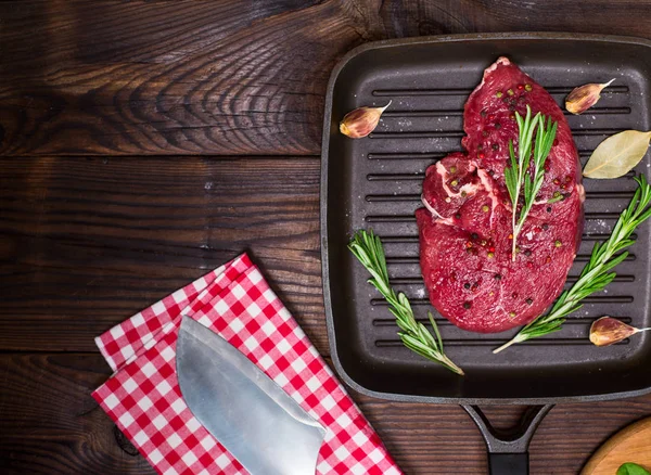 Rauwe biefstuk in specerijen op een zwarte koekenpan — Stockfoto