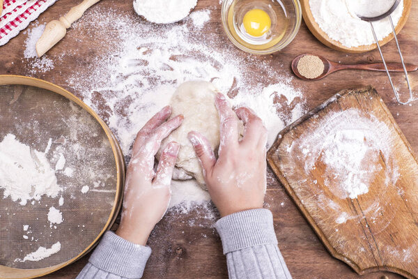 two female hands interfere with a ball of yeast dough 