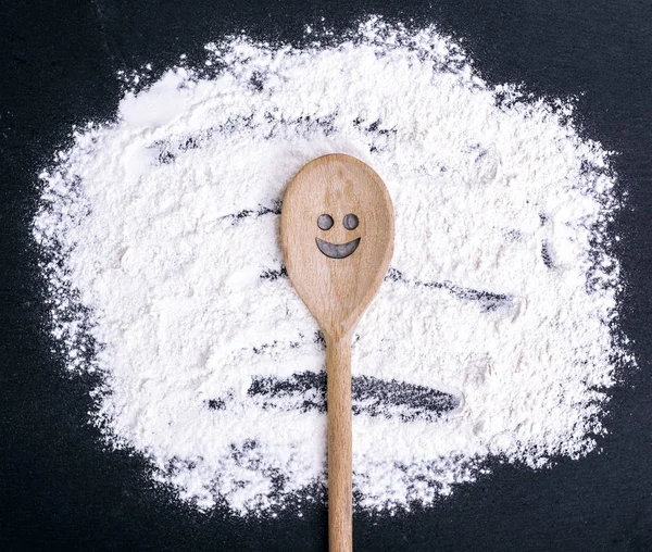 Spoon with a carved smiling face lies on scattered flour — Stock Photo, Image
