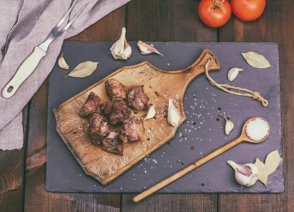 Pedaços de porco frito em uma tábua de madeira marrom com especiarias — Fotografia de Stock