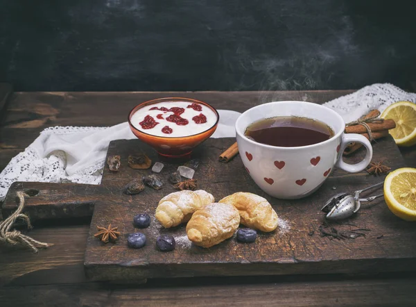 Taza blanca de cerámica con té caliente, croissants y yogur — Foto de Stock