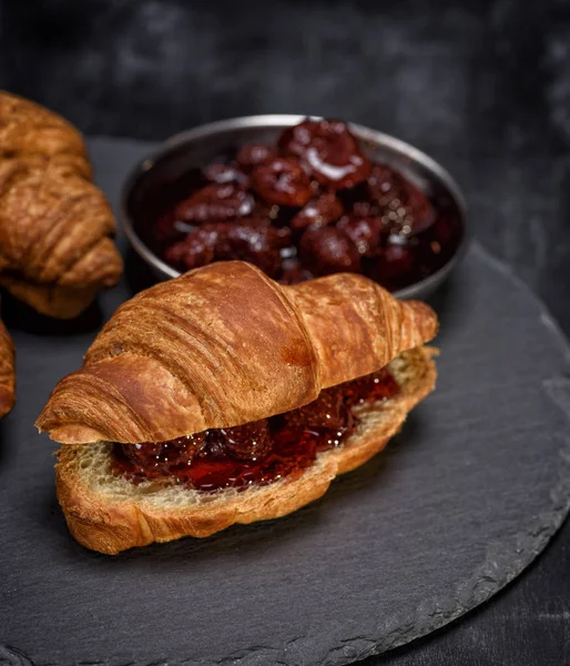 Baked croissant with strawberry jam on a black background — Stock Photo, Image