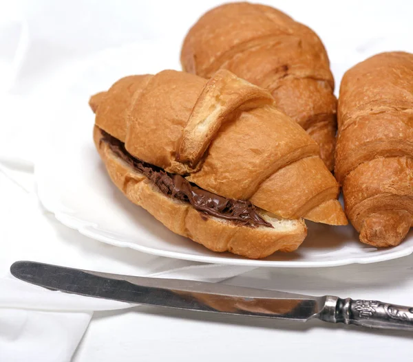 Croissants cozidos no forno com chocolate em uma placa cerâmica branca — Fotografia de Stock