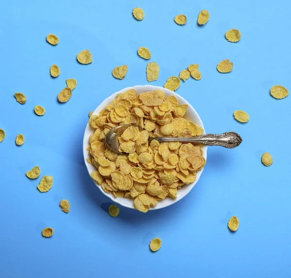 Cornflakes in a white ceramic plate and an iron spoon — Stock Photo, Image