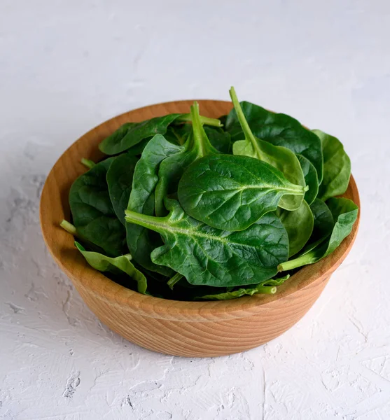 Grön spenat bladen i en brun trä skål på en vit yta, — Stockfoto