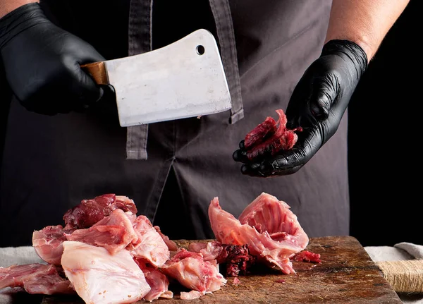 Chef em pedaços de látex preto corta em pedaços de carne crua de coelho em um — Fotografia de Stock