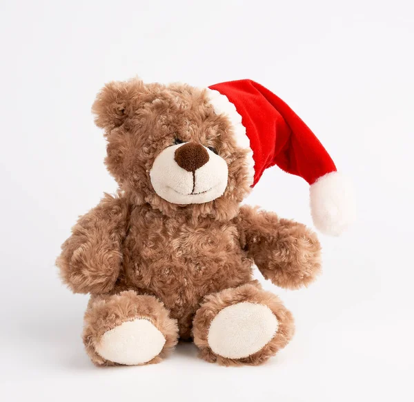 Милый коричневый плюшевый мишка в красной рождественской шляпе сидит — стоковое фото