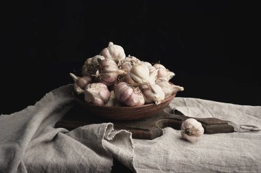 Kahverengi seramik tabakta soyulmamış sarımsak, gri keten bir şekerleme.