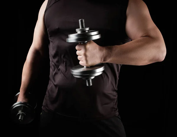 Hombre con ropa negra sostiene pesas de acero en sus manos — Foto de Stock