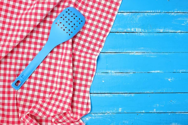 Plastic blauwe lepel met gaten op een rode textiel servet — Stockfoto