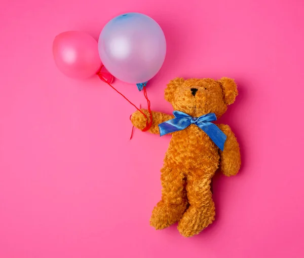 little brown teddy bear holds two inflated balloons on a rope
