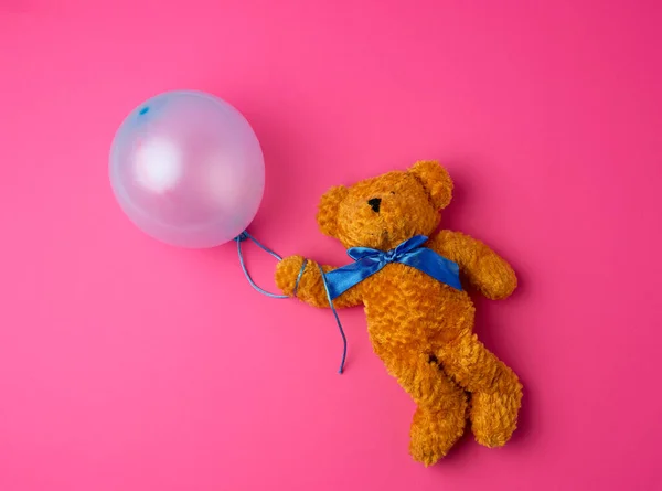 little brown teddy bear holding a blue inflated balloon