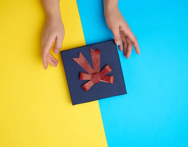 Dos manos femeninas sostienen una caja de cartón de papel azul oscuro cerrada ingenio —  Fotos de Stock